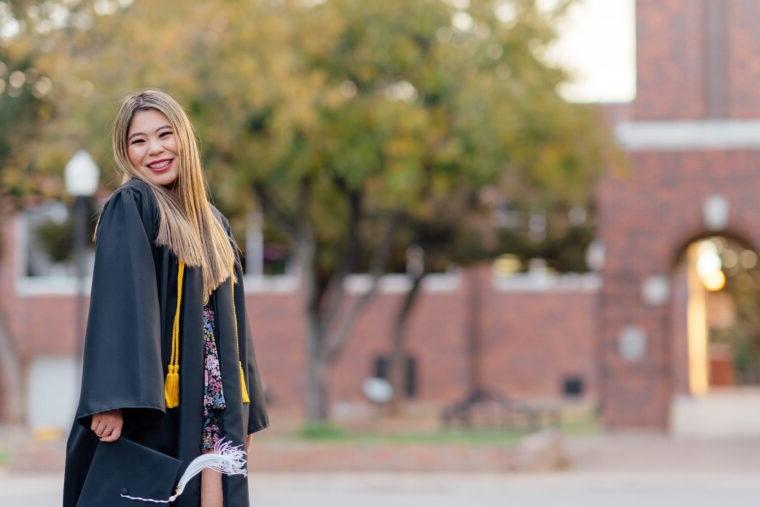 Emily Uhl in her graduation gown stands in front of the clock tower on campus.
